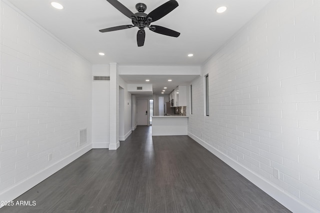 unfurnished living room featuring dark hardwood / wood-style floors, ceiling fan, and brick wall