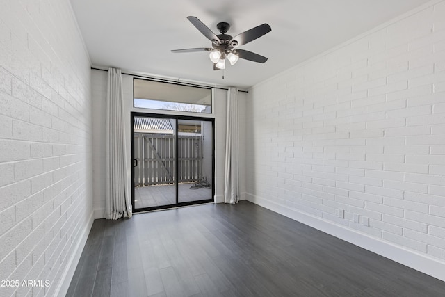 empty room with ceiling fan, brick wall, and dark hardwood / wood-style flooring