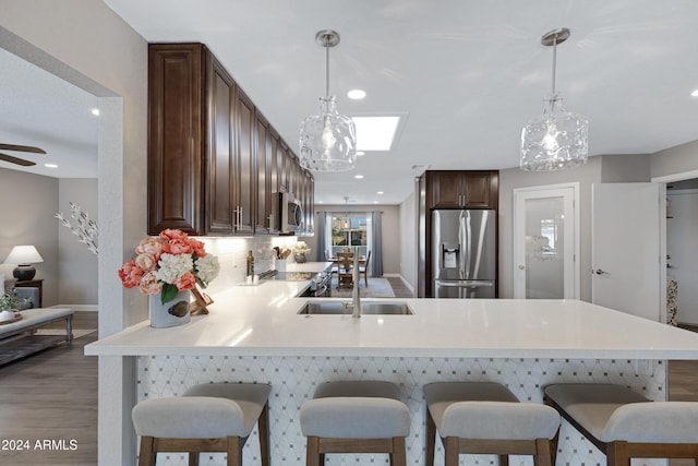 kitchen with decorative backsplash, dark hardwood / wood-style floors, kitchen peninsula, decorative light fixtures, and appliances with stainless steel finishes