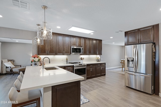 kitchen featuring appliances with stainless steel finishes, sink, a breakfast bar, hanging light fixtures, and light hardwood / wood-style flooring