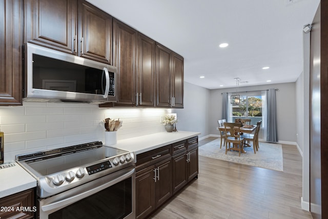 kitchen featuring hanging light fixtures, backsplash, dark brown cabinetry, appliances with stainless steel finishes, and light hardwood / wood-style floors