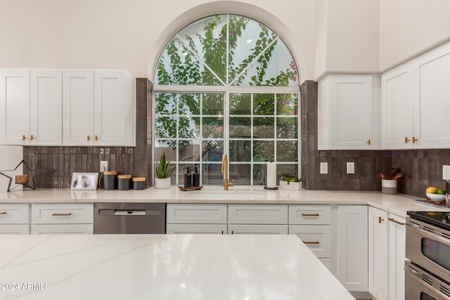 kitchen with light stone counters, white cabinets, decorative backsplash, sink, and appliances with stainless steel finishes