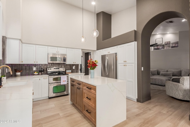 kitchen featuring white cabinets, hanging light fixtures, sink, appliances with stainless steel finishes, and a high ceiling