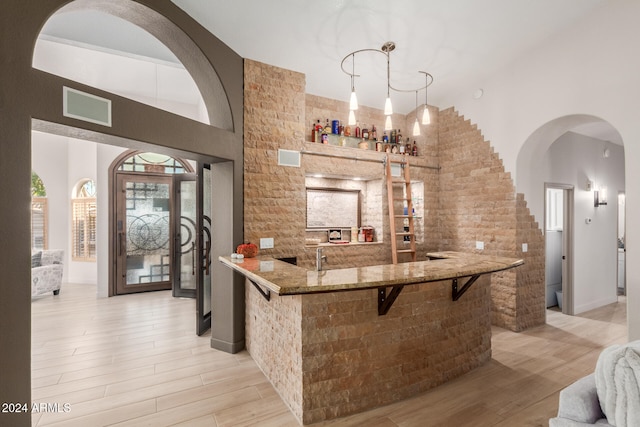 bar with light hardwood / wood-style flooring, hanging light fixtures, and stone countertops