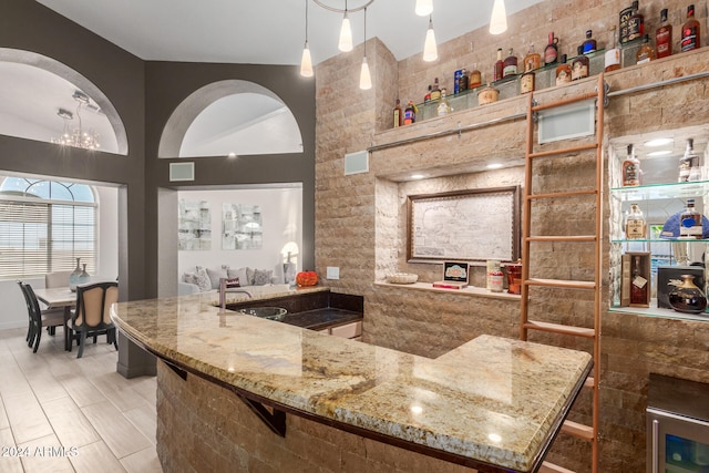 bar featuring hanging light fixtures, light stone countertops, sink, and tile walls