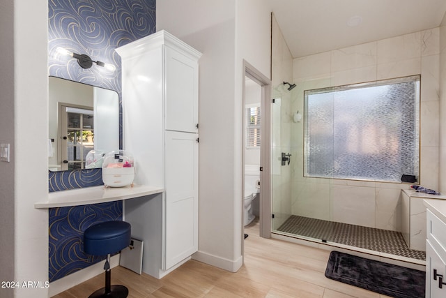 bathroom with hardwood / wood-style floors, vanity, toilet, and a tile shower