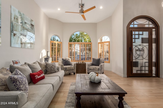 living room with a towering ceiling, light hardwood / wood-style flooring, and ceiling fan