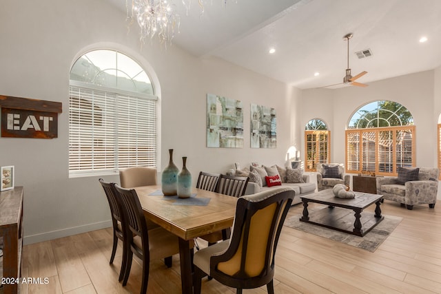 dining room with ceiling fan with notable chandelier, light hardwood / wood-style flooring, and a high ceiling