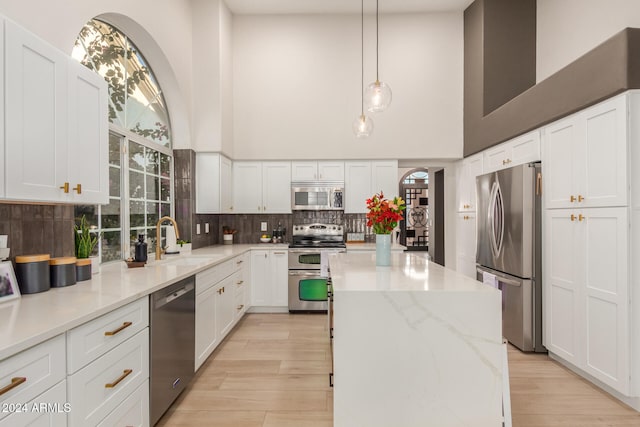 kitchen with white cabinetry, a towering ceiling, appliances with stainless steel finishes, and sink