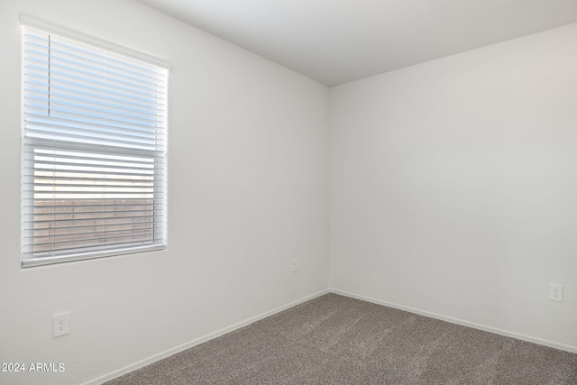 empty room featuring a wealth of natural light, baseboards, and dark carpet