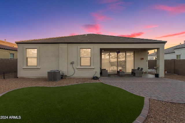 back house at dusk with central AC unit, a yard, and a patio