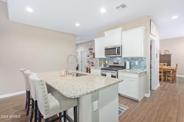 kitchen with a center island with sink, stainless steel appliances, white cabinetry, dark hardwood / wood-style floors, and sink