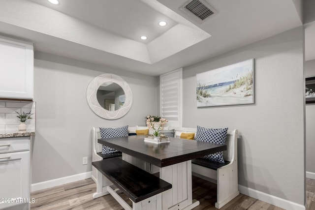 dining area with breakfast area, light hardwood / wood-style floors, and a raised ceiling