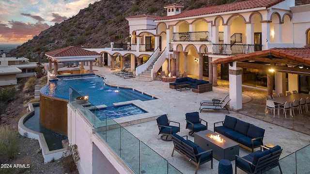 pool at dusk with a patio, an in ground hot tub, a gazebo, a mountain view, and an outdoor living space with a fire pit