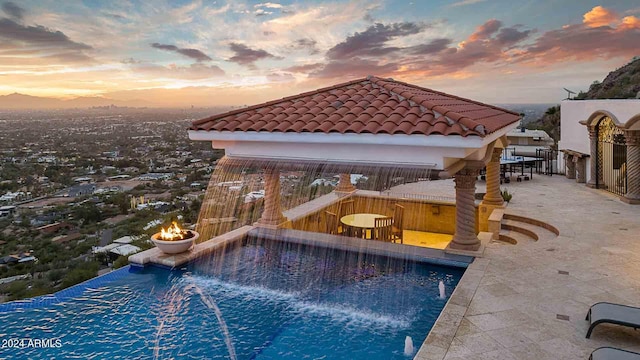 pool at dusk featuring a patio area and pool water feature