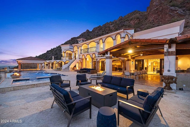 patio terrace at dusk with an outdoor living space with a fire pit, a swimming pool with hot tub, and a mountain view