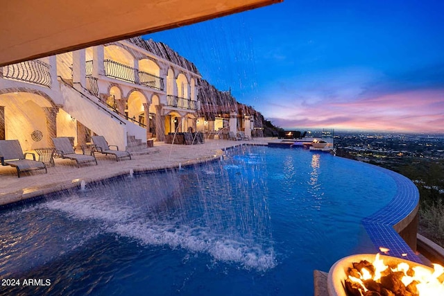 pool at dusk featuring a water view and an outdoor fire pit