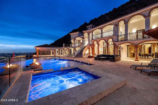 pool at dusk with a patio and an in ground hot tub