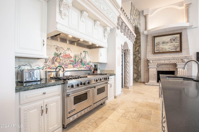 kitchen featuring sink, white cabinetry, range with two ovens, backsplash, and dark stone countertops