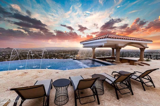 pool at dusk with a gazebo, a patio area, and pool water feature