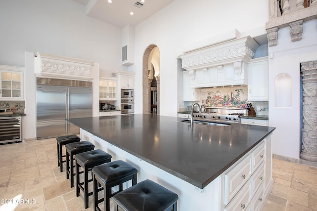 kitchen with a towering ceiling, white cabinetry, built in appliances, and wine cooler