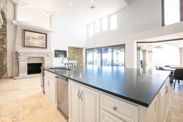 kitchen with a towering ceiling, an island with sink, white cabinets, dishwasher, and sink