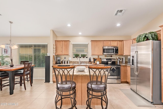 kitchen with light tile patterned flooring, a kitchen island, appliances with stainless steel finishes, sink, and light stone counters