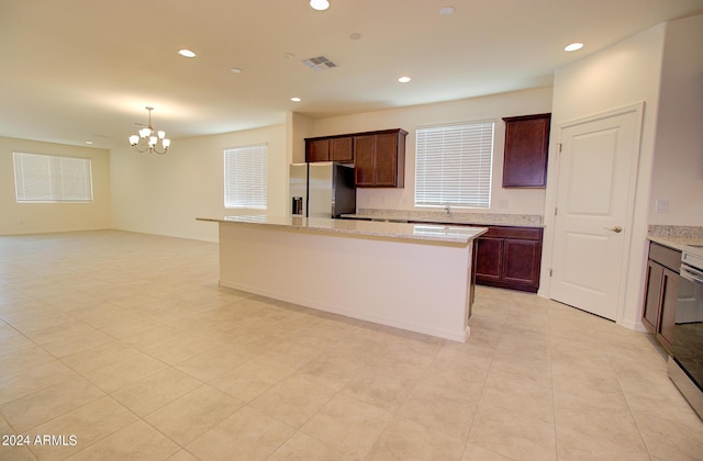 kitchen with pendant lighting, a center island, an inviting chandelier, stainless steel fridge, and light stone counters