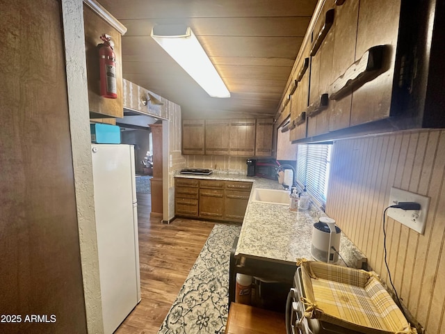 kitchen with wooden walls, light wood finished floors, freestanding refrigerator, a sink, and light countertops