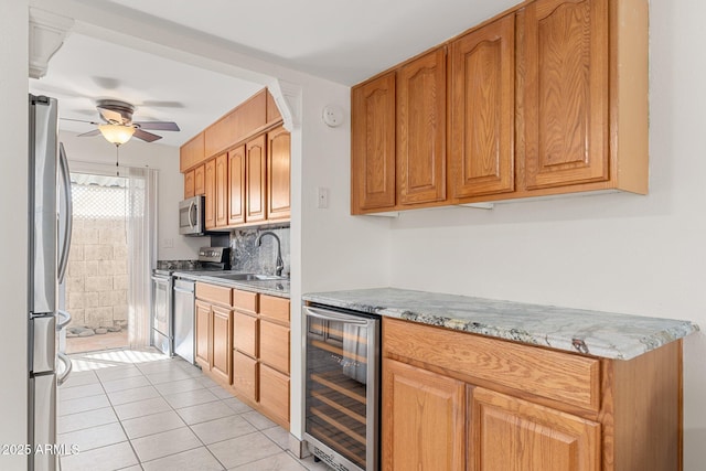 kitchen featuring appliances with stainless steel finishes, light tile patterned flooring, beverage cooler, light stone countertops, and sink