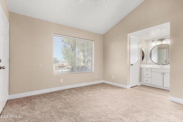 unfurnished bedroom featuring light colored carpet, ensuite bath, lofted ceiling, and sink