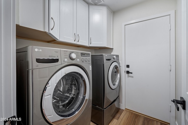 washroom featuring washing machine and clothes dryer, hardwood / wood-style floors, and cabinets