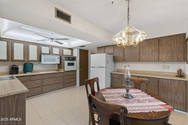 kitchen with light tile patterned floors, white appliances, sink, ceiling fan with notable chandelier, and decorative light fixtures