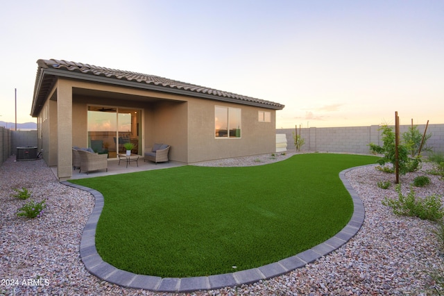 back house at dusk featuring outdoor lounge area, a yard, a patio, and central air condition unit