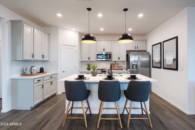 kitchen featuring appliances with stainless steel finishes, decorative light fixtures, dark hardwood / wood-style floors, and a center island with sink