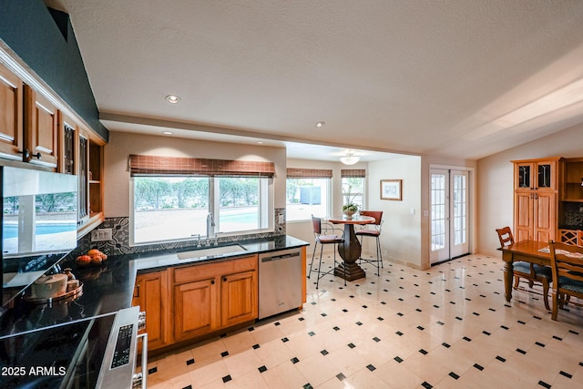 kitchen with french doors, dark countertops, brown cabinetry, a sink, and dishwasher