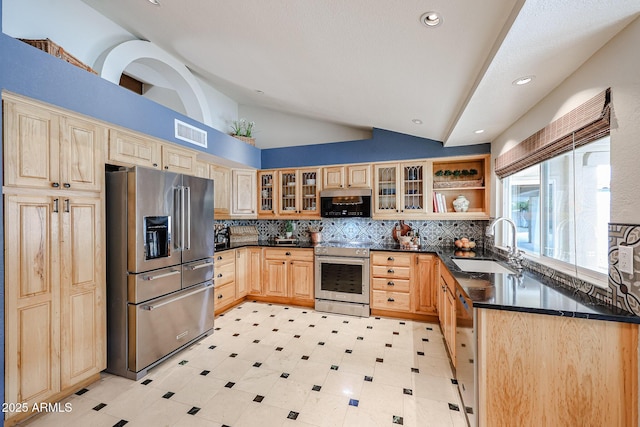 kitchen featuring light brown cabinetry, appliances with stainless steel finishes, dark countertops, and a sink