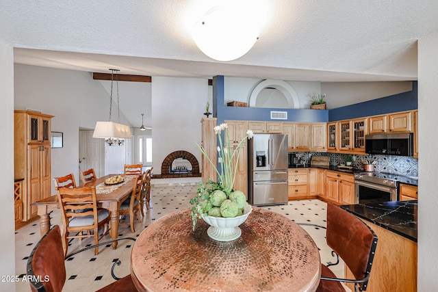 kitchen with tasteful backsplash, dark countertops, appliances with stainless steel finishes, glass insert cabinets, and vaulted ceiling