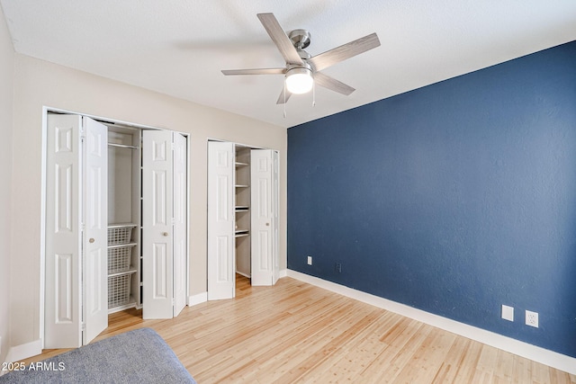 unfurnished bedroom with multiple closets, a ceiling fan, baseboards, and wood finished floors