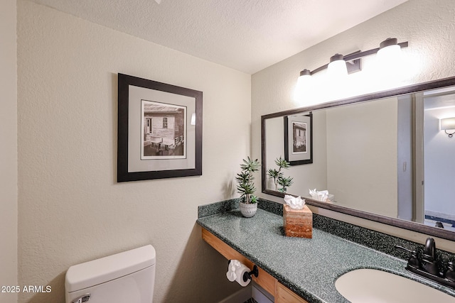 half bathroom with a textured ceiling, a textured wall, vanity, and toilet