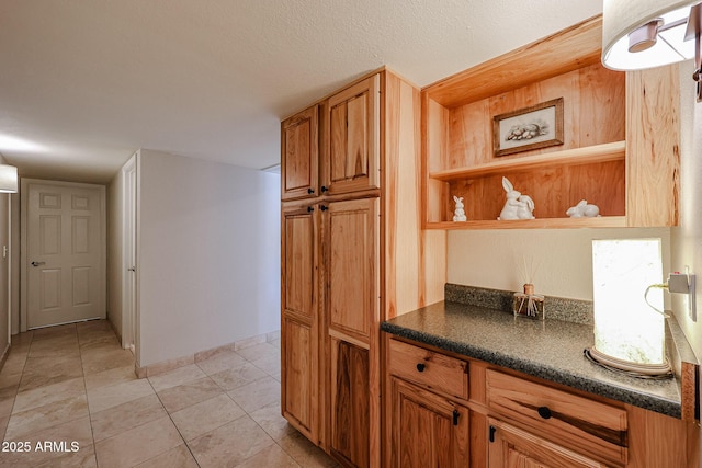 kitchen featuring dark countertops, a textured ceiling, baseboards, and light tile patterned floors