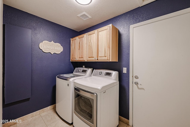 laundry room featuring a textured wall, washer and clothes dryer, light tile patterned flooring, and cabinet space