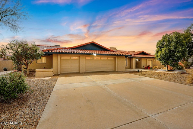 view of front of property featuring concrete driveway, an attached garage, a tiled roof, and stucco siding