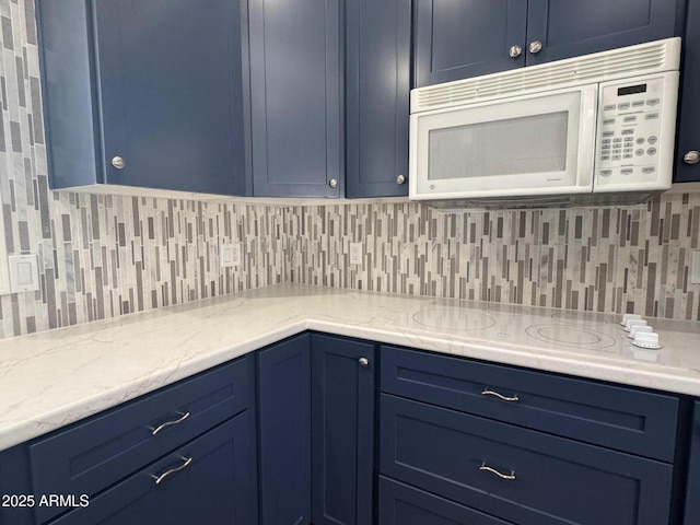 kitchen featuring white microwave, electric cooktop, blue cabinetry, light stone countertops, and tasteful backsplash