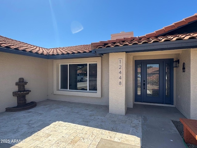 property entrance featuring a patio area, a tile roof, and stucco siding