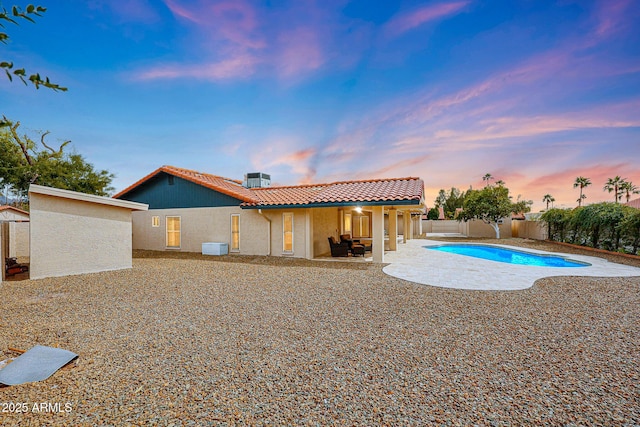 back of property at dusk featuring a fenced in pool, stucco siding, a patio area, a fenced backyard, and a tiled roof