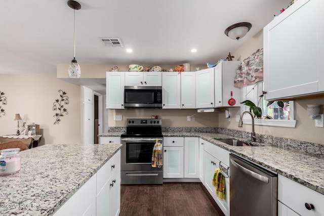 kitchen with light stone countertops, appliances with stainless steel finishes, a sink, white cabinetry, and dark wood-type flooring
