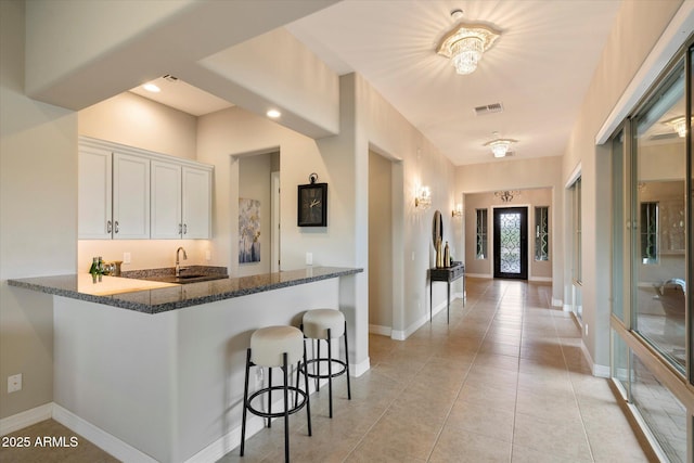 8597 E Arroyo Seco Rd, Scottsdale, AZ 85266 - kitchen with white cabinets, a kitchen breakfast bar, dark stone countertops, visible vents, and a sink