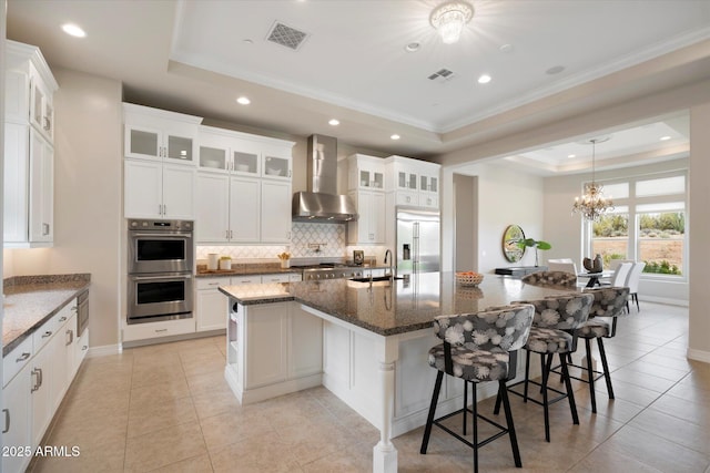 8597 E Arroyo Seco Rd, Scottsdale, AZ 85266 - kitchen with stainless steel appliances, a tray ceiling, a sink, visible vents, and wall chimney range hood