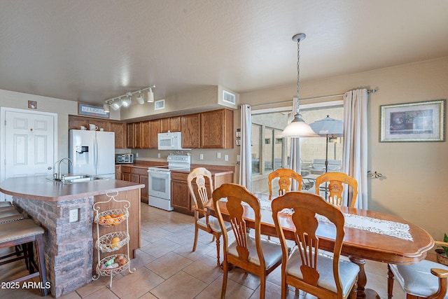 kitchen featuring sink, light tile patterned floors, pendant lighting, white appliances, and a kitchen island with sink